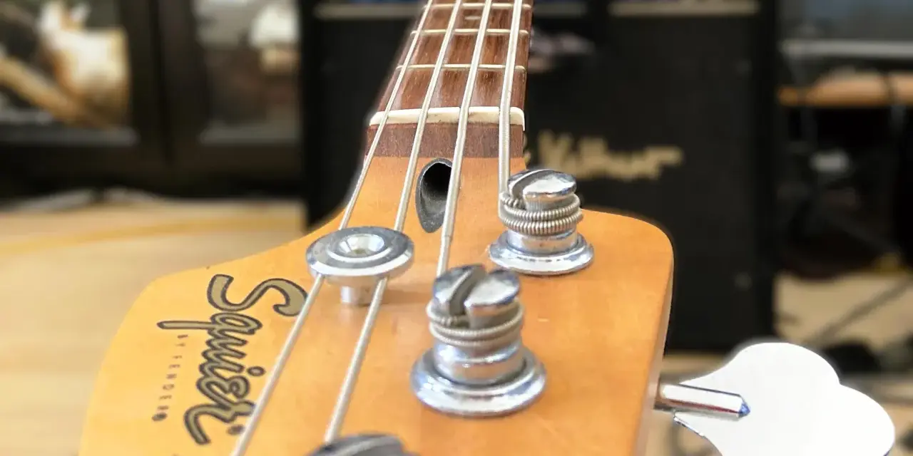 Nahaufnahme des Bass-Kopfes mit Saiten und Stimmmechaniken. Der Schriftzug "Squier by Fender Jazz Bass" ist sichtbar. Perfekt, um den Bass einzustellen.