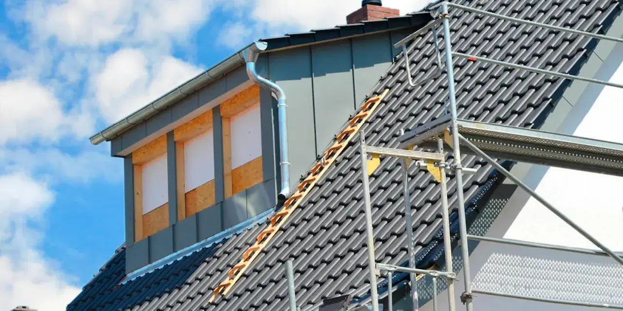 Bygga takkupa pågår. Ett hus med takpannor och byggställning, en ny takkupa med fönsteröppningar syns.