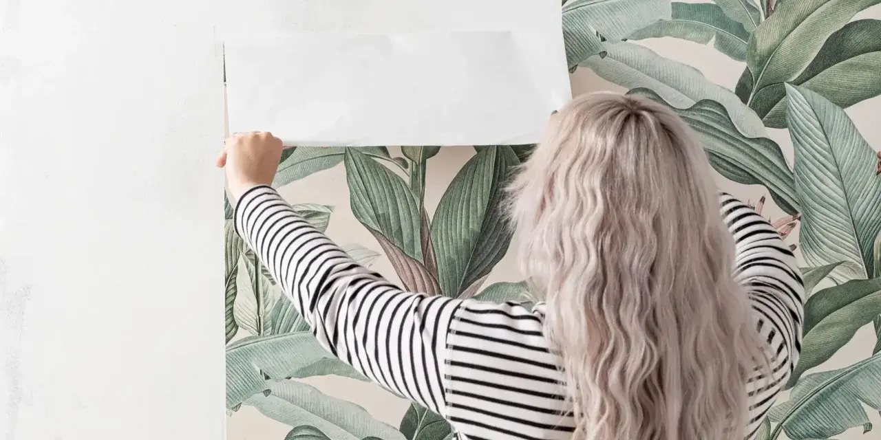 En kvinna med blont hår håller på att ta bort tapet med ett tropiskt mönster.