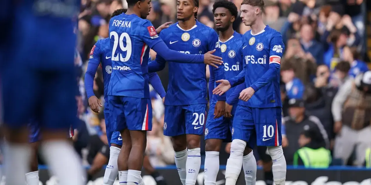 Piłkarze Chelsea w niebieskich strojach rozmawiają na boisku. Widać numery 29, 20 i 10.