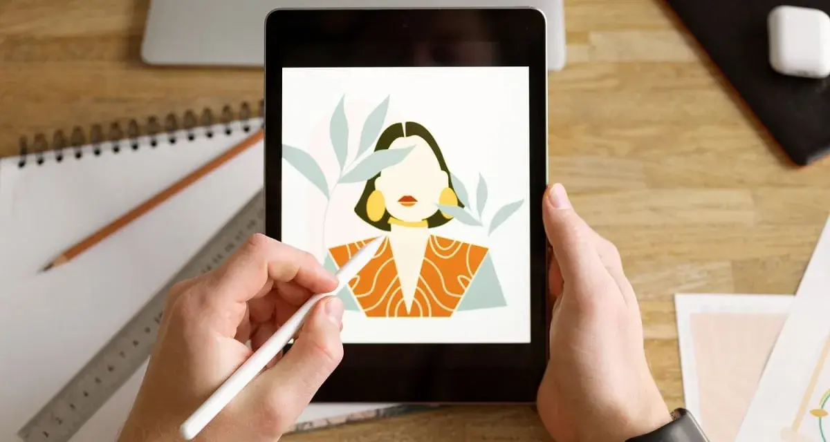 Ręce trzymają tablet z rysunkiem kobiety, tworzonym w aplikacji procreate. Obok leżą szkicownik i ołówek.