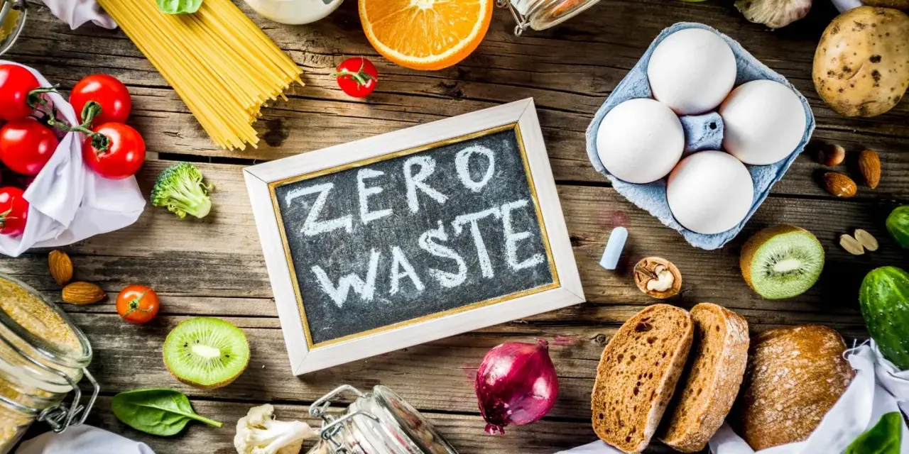 Tablica z napisem "ZERO WASTE" otoczona świeżymi warzywami, owocami, jajkami i produktami sypkimi. Styl życia bez marnowania.