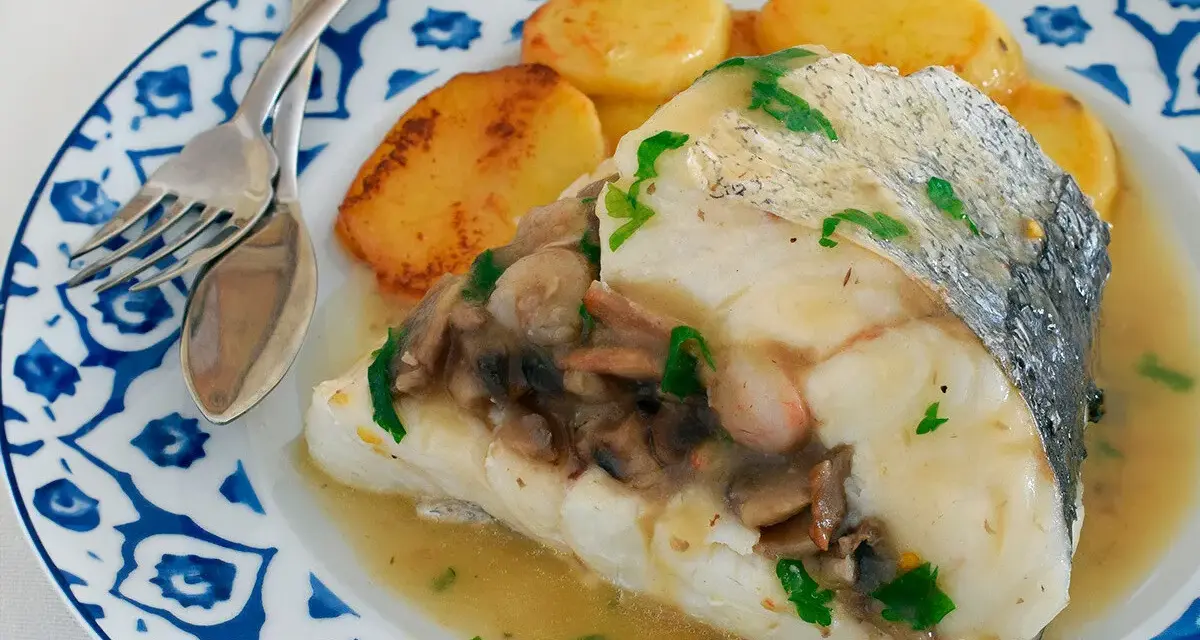Deliciosa merluza con gambas y champiñones, servida con patatas doradas en un plato azul y blanco.