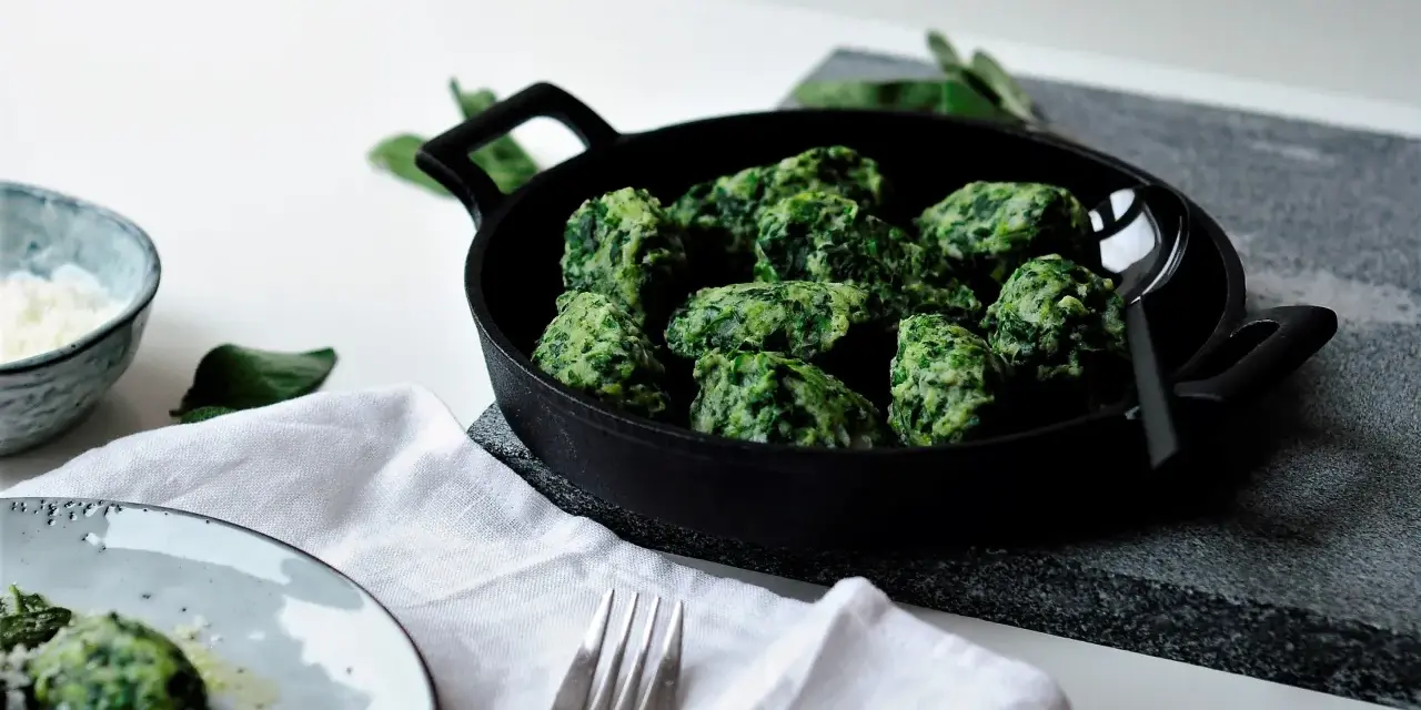 Malfatti, was ist das? Grüne, unregelmäßige Klößchen aus Spinat und Ricotta in einer Pfanne, daneben ein Teller mit mehr Malfatti und Parmesan.