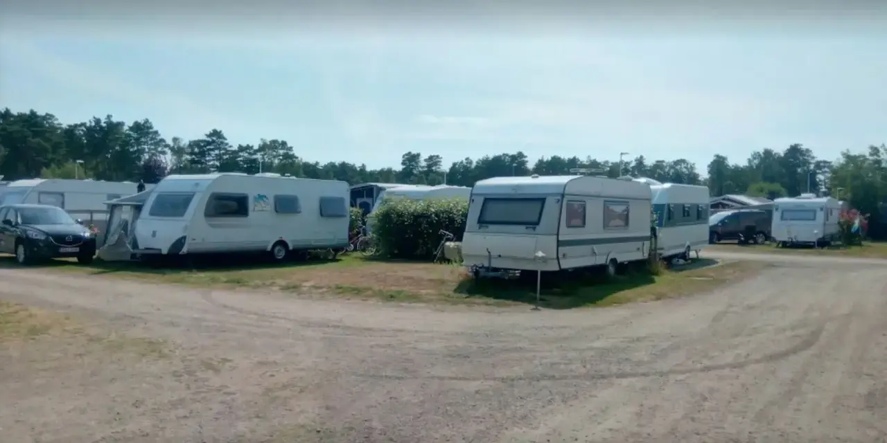 Ställplatser med husvagnar och bilar på Olles camping. Träd och blå himmel syns i bakgrunden.