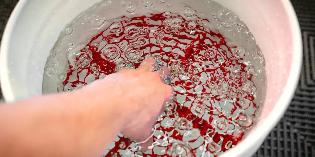 En hand rör vid vatten med röda mönster i en hink. En **grit guard** fångar upp smuts och skyddar din bils lack.