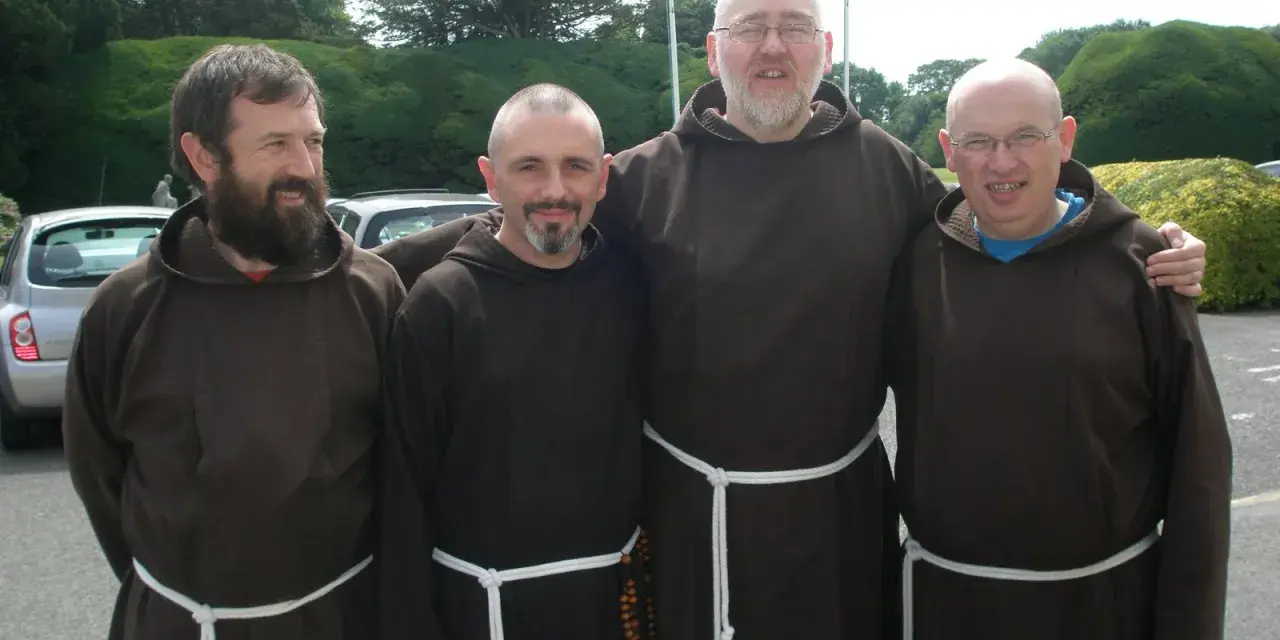 Four monk priests in brown robes stand together outdoors.