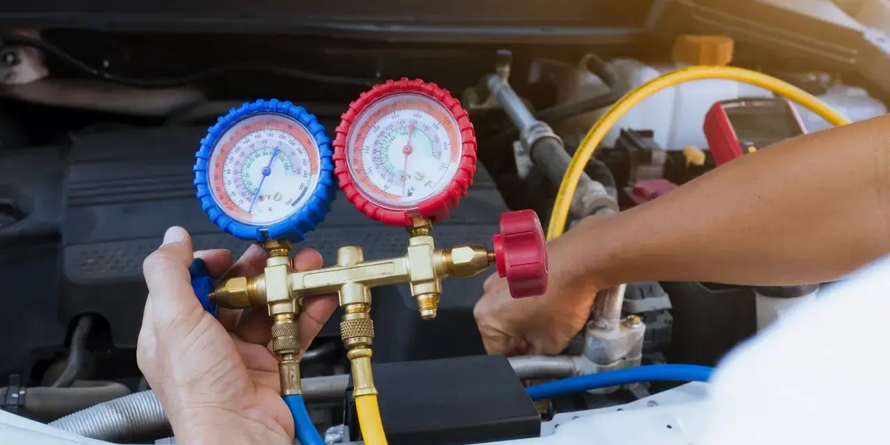 A mechanic uses a manifold gauge set to check for a freon leak in a car's AC system.