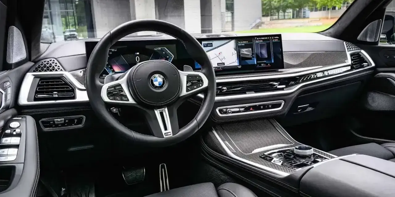 Wnętrze BMW x7: skórzana tapicerka, nowoczesny kokpit z dwoma ekranami i sportowa kierownica.