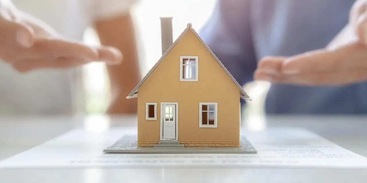 Modèle de maison sur des documents, mains en arrière-plan suggérant une solution pour sortir de l'indivision sans vendre.