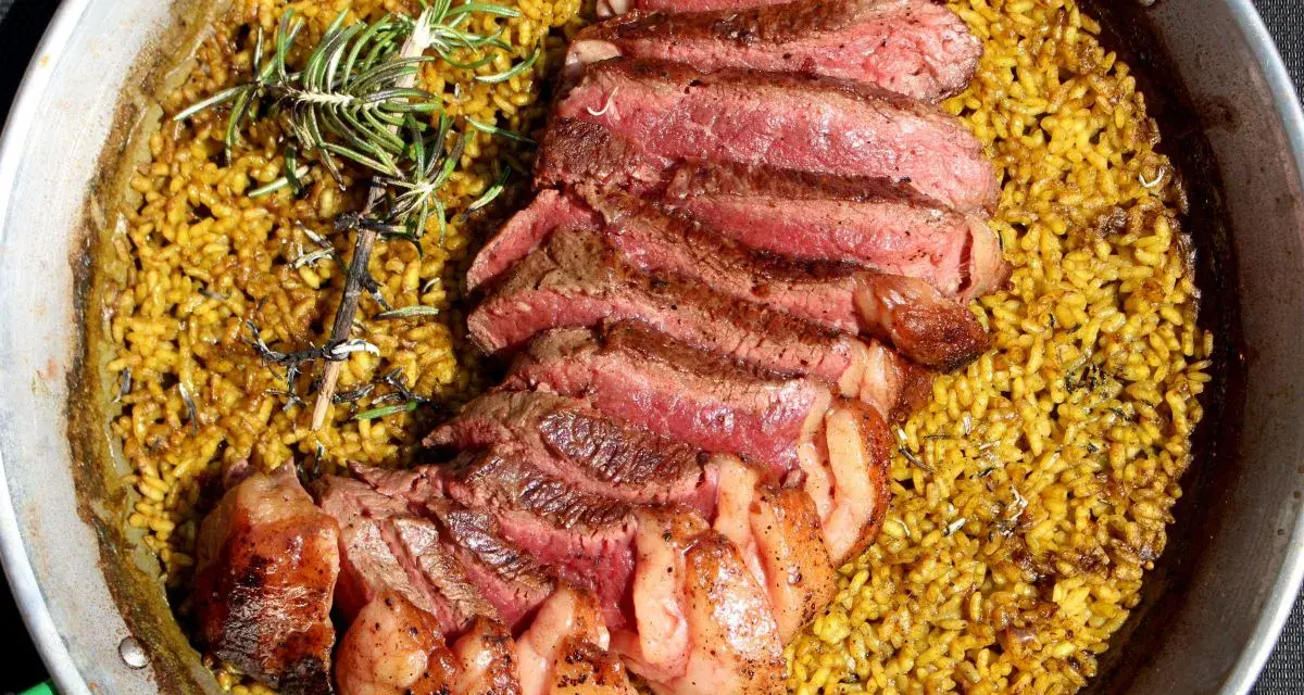 Arroz amarillo con chuletón a la parrilla y romero en paellera.