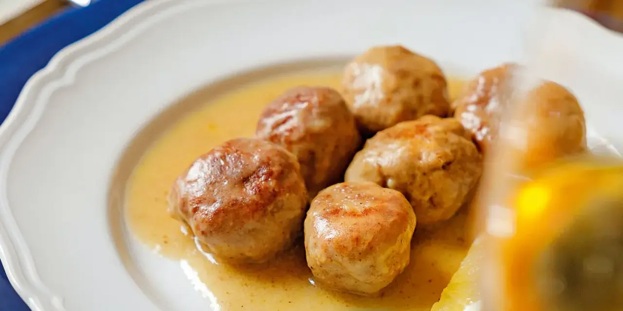 Polpette al limone succulente in un piatto bianco, con una fetta di limone e basilico.