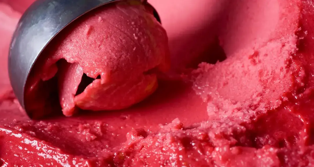 Ein Löffel nimmt eine Kugel leuchtend rotes Eis auf. Es sieht aus wie ein köstliches Blaubeereis, das zum Genießen bereit ist.