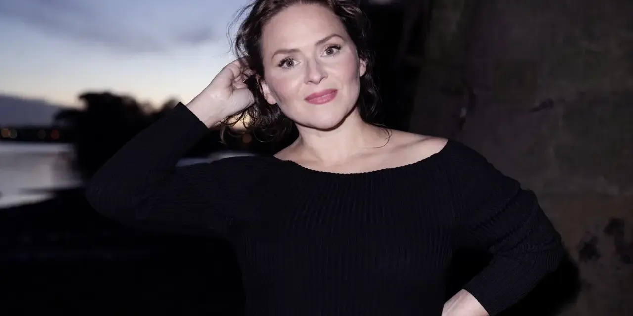 Emiliana Torrini, la chanteuse, pose au crépuscule près de l'eau, une main dans ses cheveux.