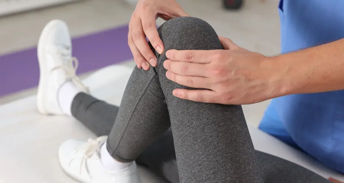 Fizjoterapeuta ocenia zakres ruchu w stawie kolanowym pacjentki, delikatnie dotykając jej nogi.