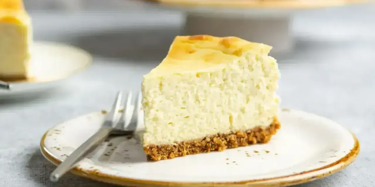 Pyszny sernik na kruchym spodzie, idealny do pieczenia w piekarniku z termoobiegiem. Kawałek na talerzyku z widelcem.