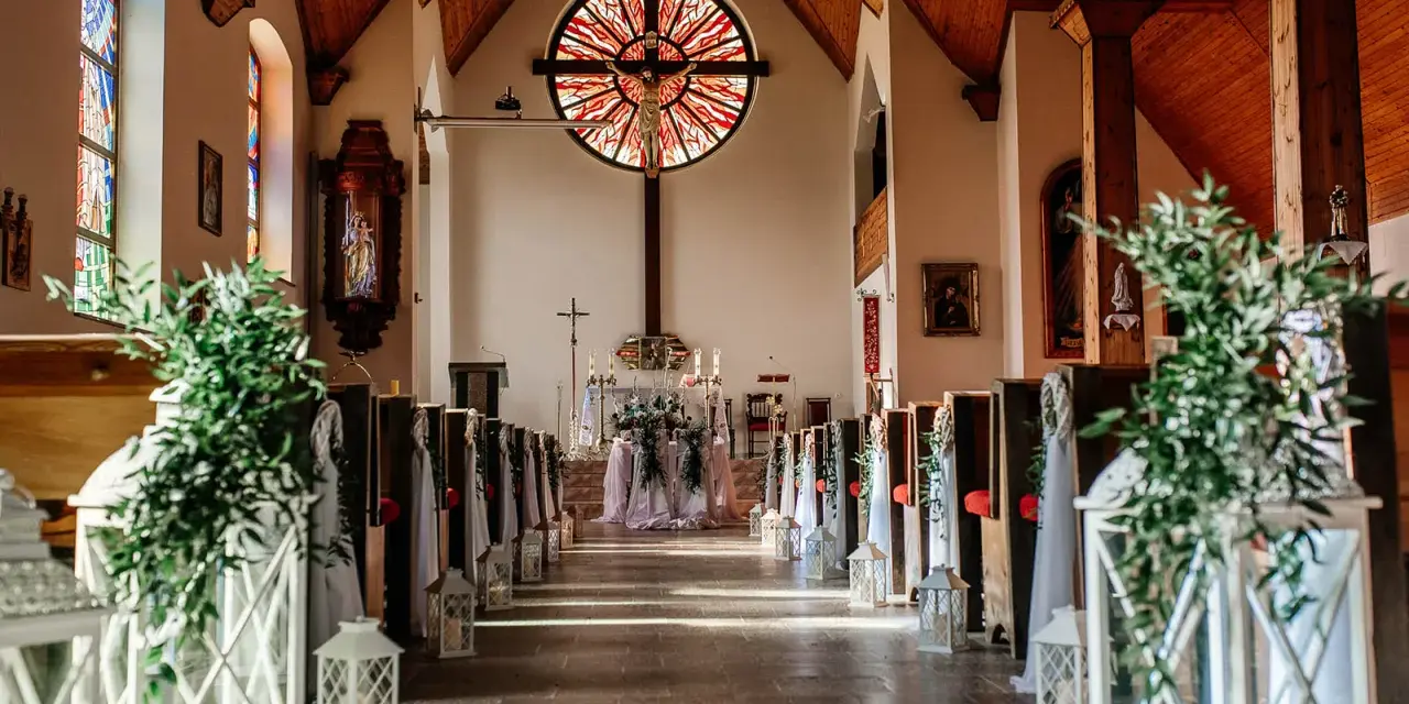 Piękna dekoracja kościoła na ślub samemu: lampiony, zielone gałązki i białe tkaniny tworzą romantyczną atmosferę.