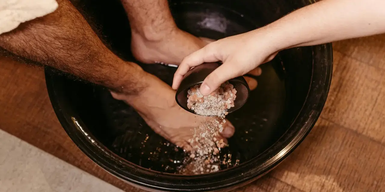A hand pours pink salt into a foot bath, adding to the foot detox ingredients for a relaxing soak.