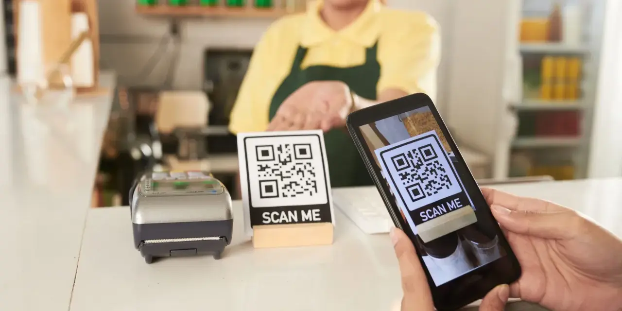 Cliente usa su móvil para escanear un código QR y hacer su carta digital. Un datáfono y otro código QR esperan en el mostrador.