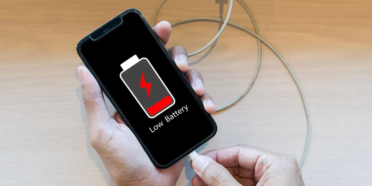 En person kopplar in sin mobil för att ladda mobilen på natten. Batteriikonen visar låg nivå.