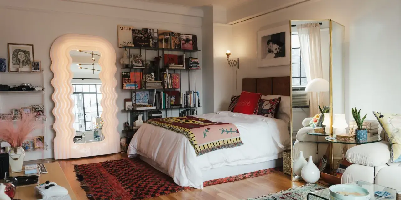 Ideas para decorar habitación estudio: cama blanca, espejo ondulado, estanterías con libros y arte, alfombras coloridas y un sofá acogedor.
