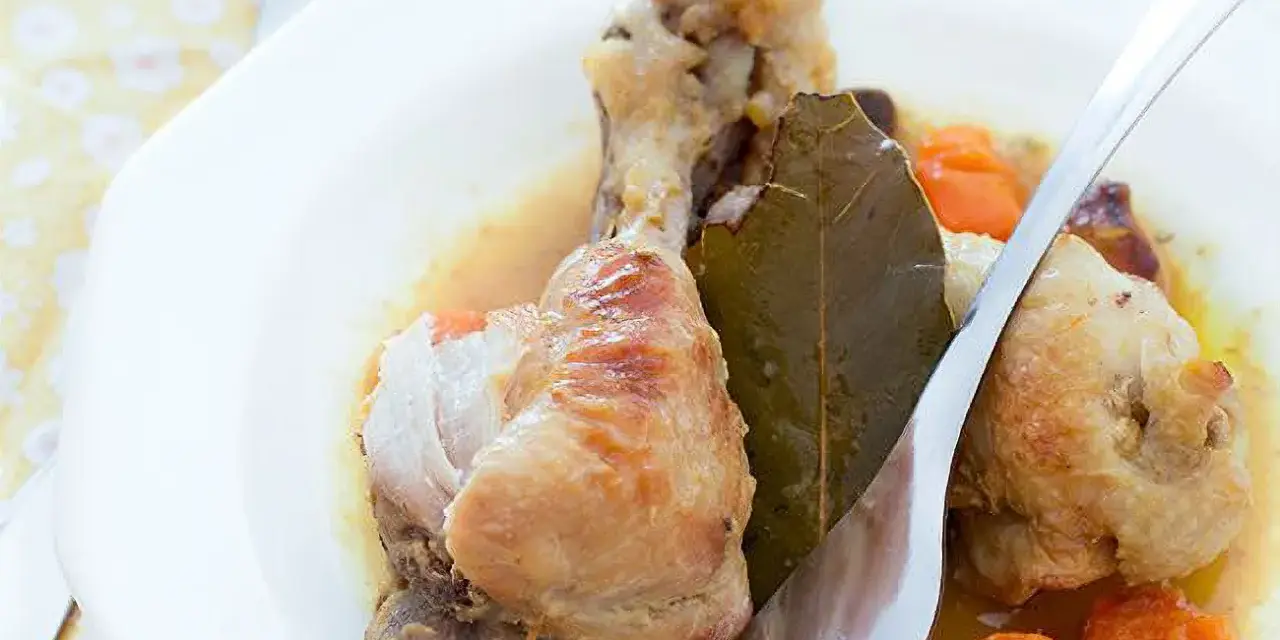 Delicioso pollo guisado con zanahorias y hoja de laurel en un plato blanco, listo para ser disfrutado.