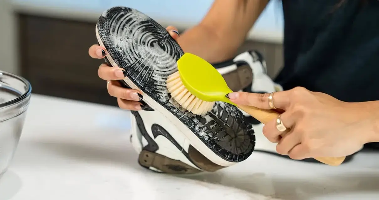 Mani che puliscono la suola di una scarpa con una spazzola gialla e schiuma. Un modo efficace per capire come pulire la suola delle scarpe.