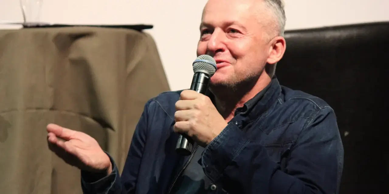 Bogusław Linda opowiada o swoich rolach w serialach i programach, trzymając mikrofon.
