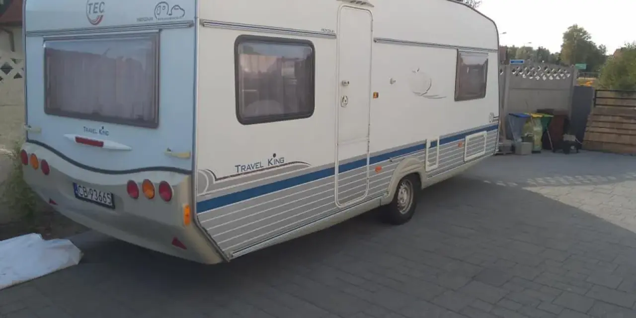 Biała przyczepa kempingowa TEC Travel King z niebieskimi pasami, gotowa na wakacyjne podróże.