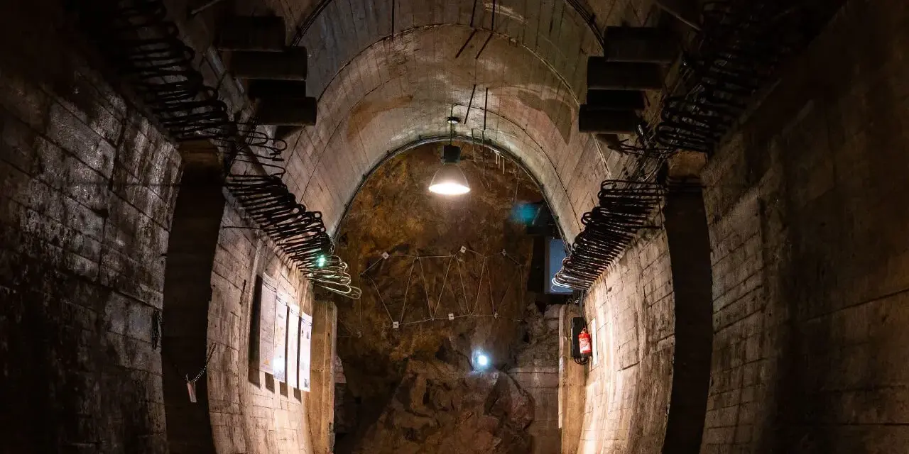 Wnętrze tunelu w Górach Sowich. Betonowe ściany, łukowe sklepienie i oświetlenie tworzą mroczny klimat.