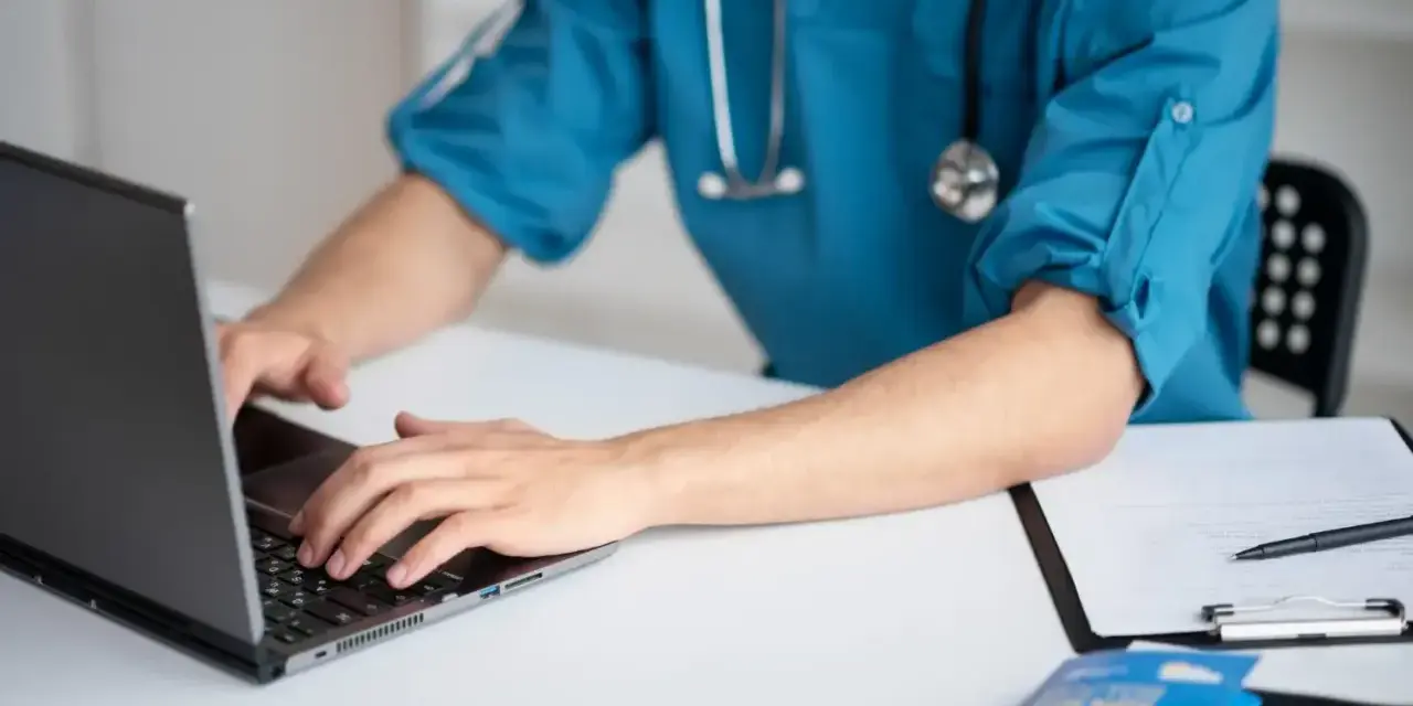 Lekarz medycyny pracy na laptopie, przygotowuje dokumentację. Zastanawiasz się, ile trwa wizyta u lekarza medycyny pracy?
