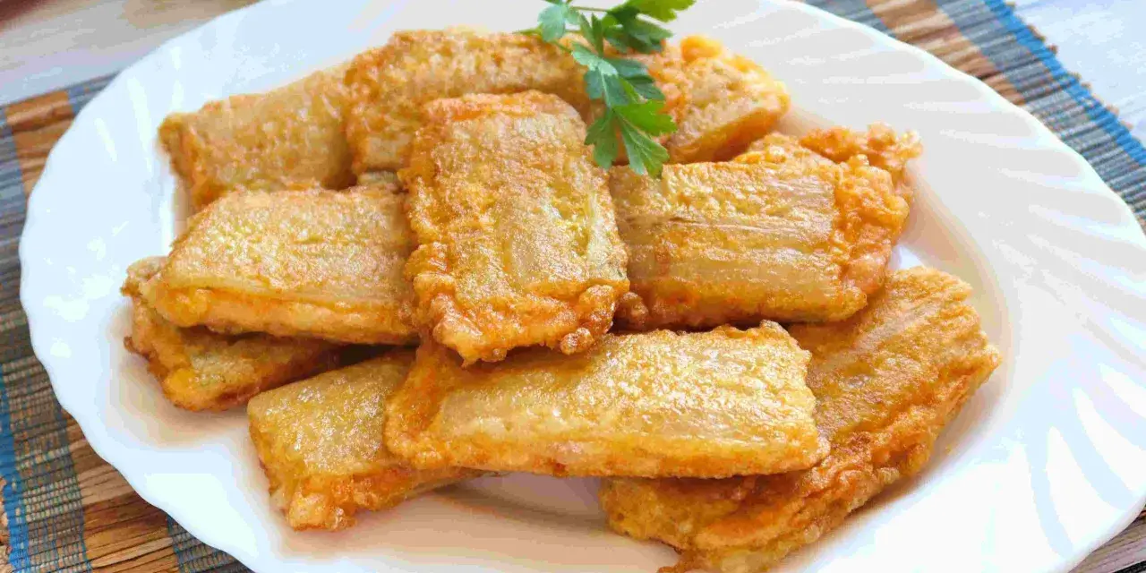 Pencas rellenas doradas y crujientes, apiladas en un plato blanco, con una ramita de perejil fresco.