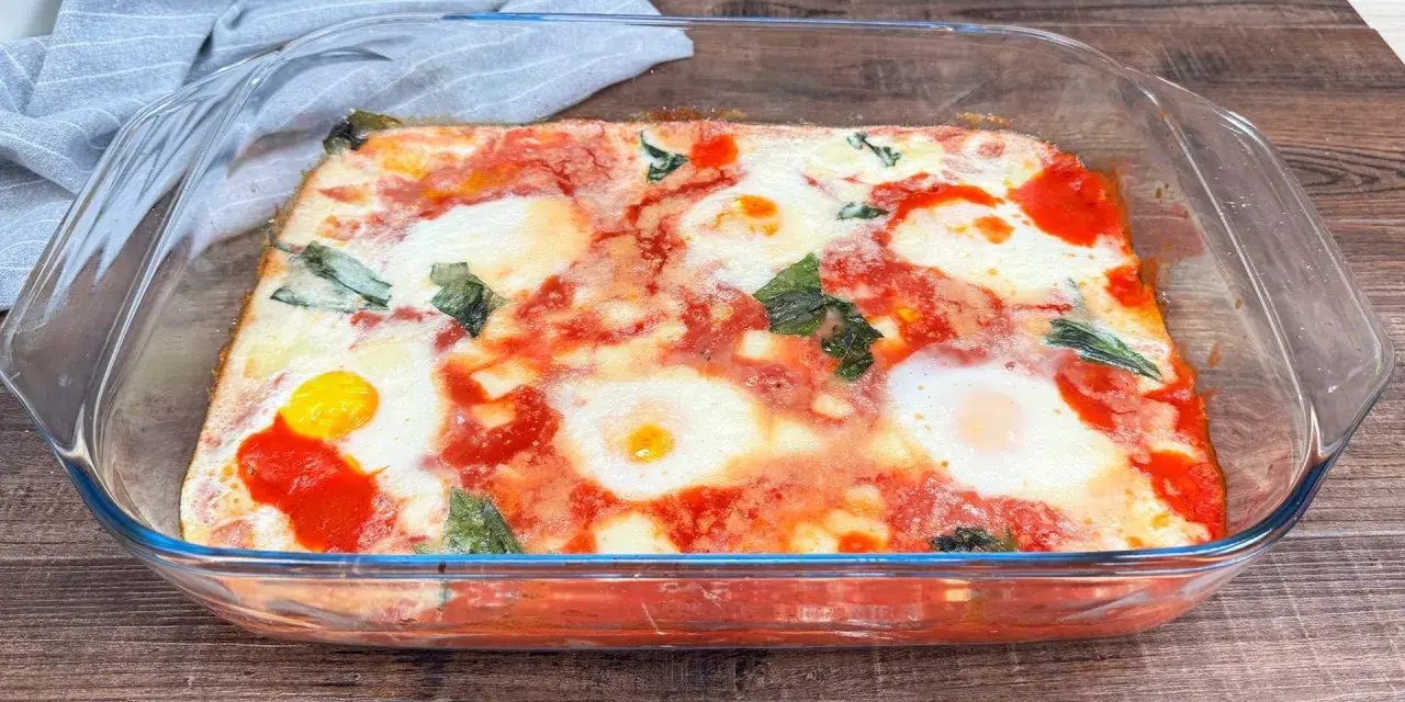 Uova alla contadina appena sfornate in teglia di vetro, con pomodoro e basilico.