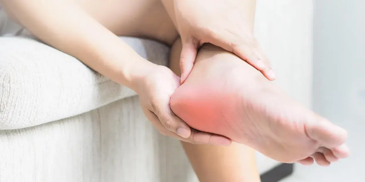 Dłoń masuje bolesną piętę, gdzie może występować neuropatia Baxtera.
