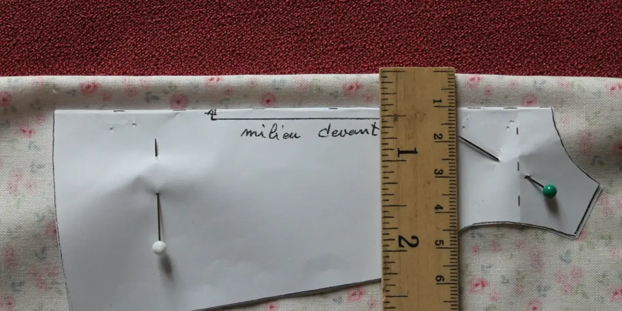 Patron de couture marqué "milieu devant", épinglé sur un tissu fleuri. Une règle en bois mesure la pièce.