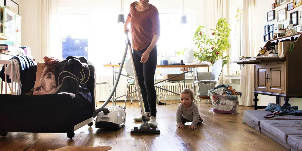 Frau saugt, Baby krabbelt. Wenn der Staubsauger stinkt, was tun? Filter wechseln oder Beutel leeren!