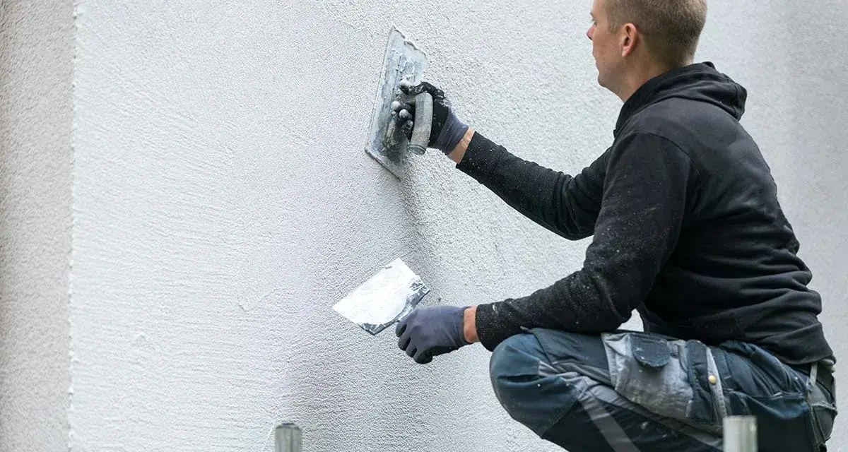 Un ouvrier applique un enduit sur un mur extérieur avec une truelle.