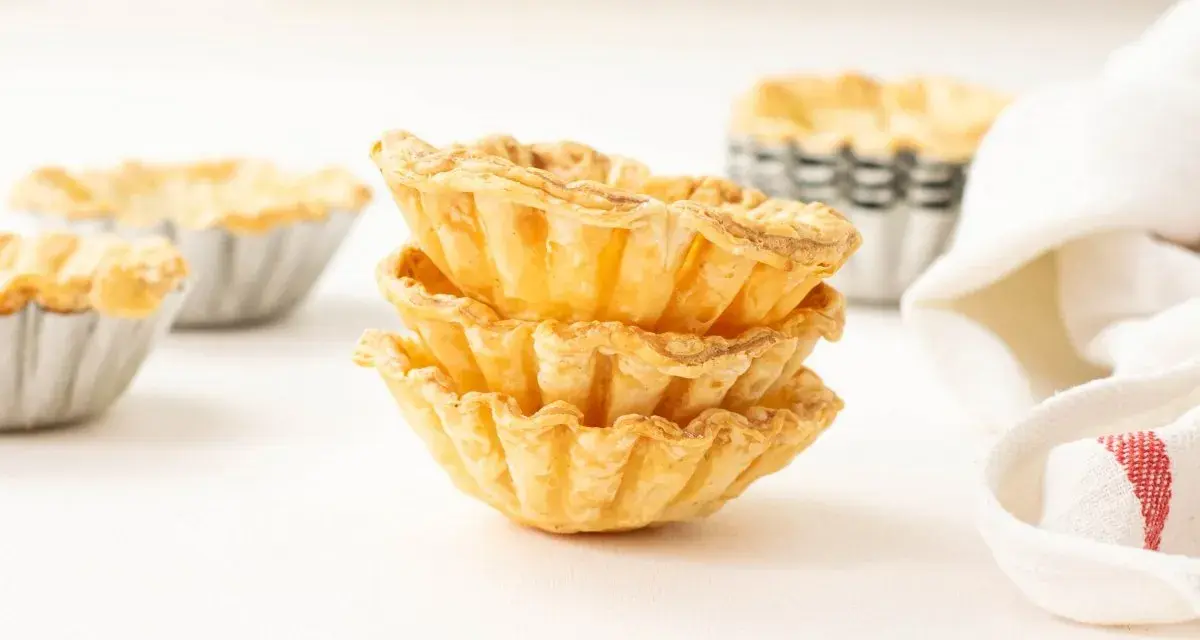 Montón de tartaletas de hojaldre listas para rellenar con crema pastelera.