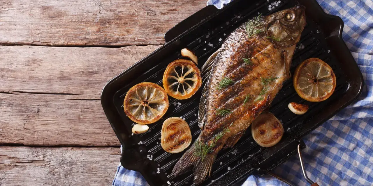 Gegrillter Karpfen mit Zitronenscheiben und Kräutern auf einer Grillpfanne. Ein Genuss, Karpfen zu essen!