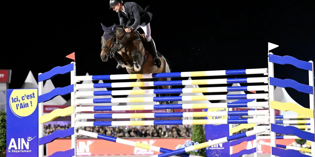 Cavalier et cheval en plein saut lors de l'épreuve des 6 barres. Le cheval est au sommet de son effort, les pattes repliées, franchissant l'obstacle.