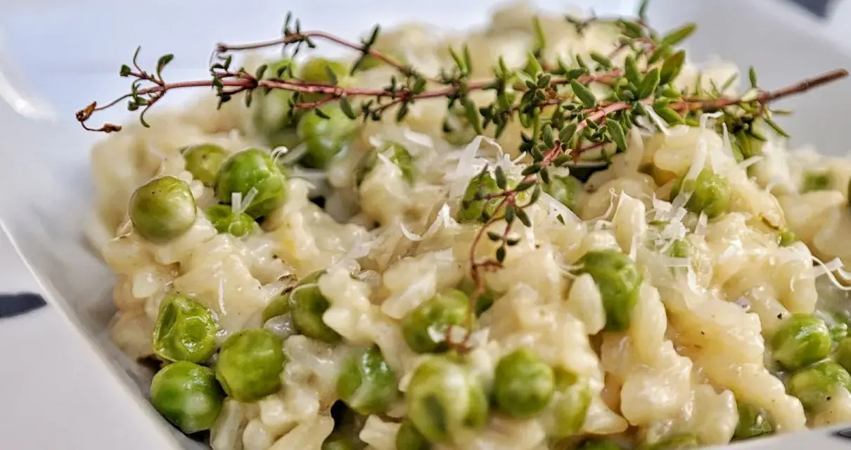 Kremowe risotto z groszkiem, posypane parmezanem i udekorowane gałązką tymianku. Pyszne danie, które zachwyca smakiem.