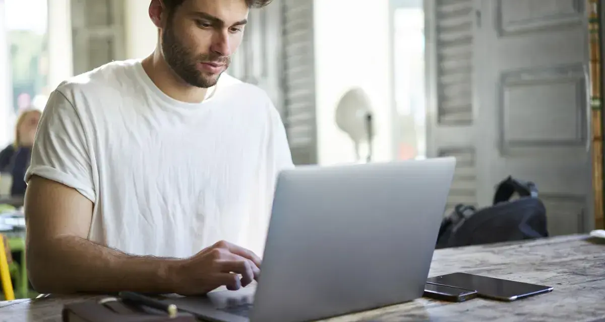 Mężczyzna w białej koszulce pisze na laptopie, przygotowując wniosek o urlop na poszukiwanie pracy.