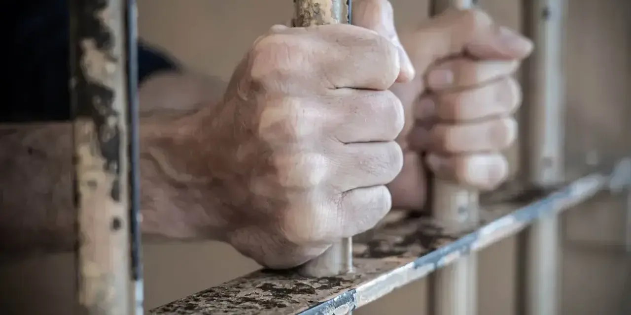 Dłonie zaciskają się na kratach więziennych. Dowiedz się, jak skontaktować się z osadzonym, szukając informacji o odwiedzinach i korespondencji.