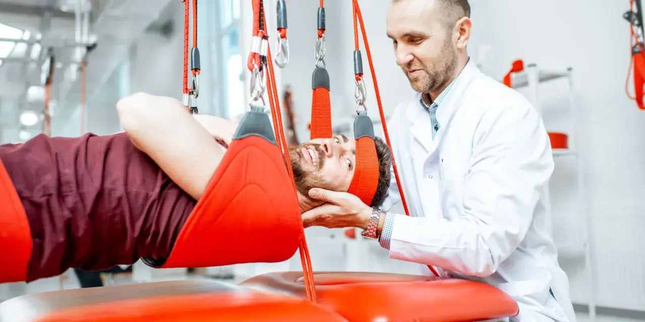 Fizjoterapeuta pomaga pacjentowi w terapii wiszącej, która może być jednym z zabiegów rehabilitacyjnych na kręgosłup lędźwiowy.