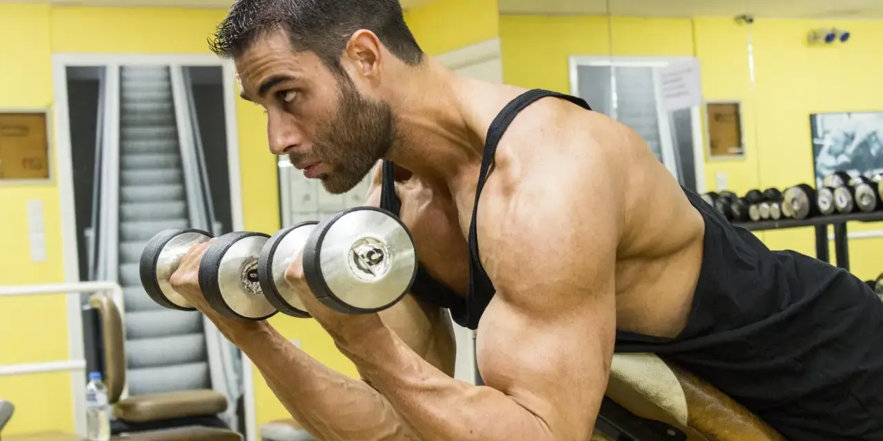 Man utför spider curls med hantlar på ett gym.