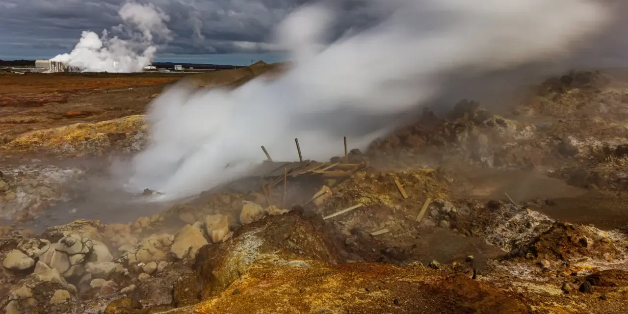 Gunnuhver hot springs: para buchująca z ziemi, zniszczona drewniana konstrukcja, chmury burzowe nad krajobrazem.