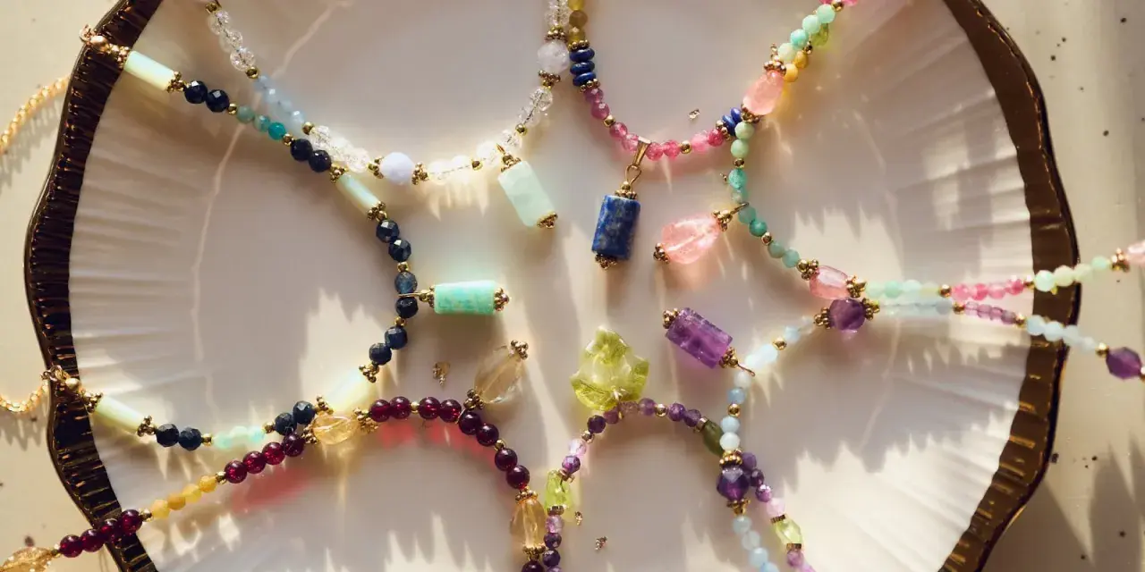 Kolorowe naszyjniki z kamieni szlachetnych, w tym lapis lazuli znak zodiaku, ułożone na talerzu.