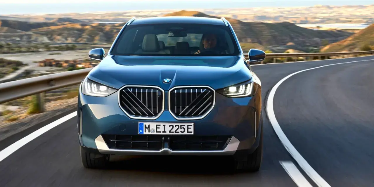 Nowy **BMW X3 2025** w kolorze granatowym jedzie krętą drogą pośród pustynnych krajobrazów.