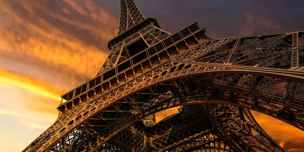 La Torre Eiffel, una icónica estructura de hierro forjado, se alza majestuosa contra un cielo anaranjado al atardecer.