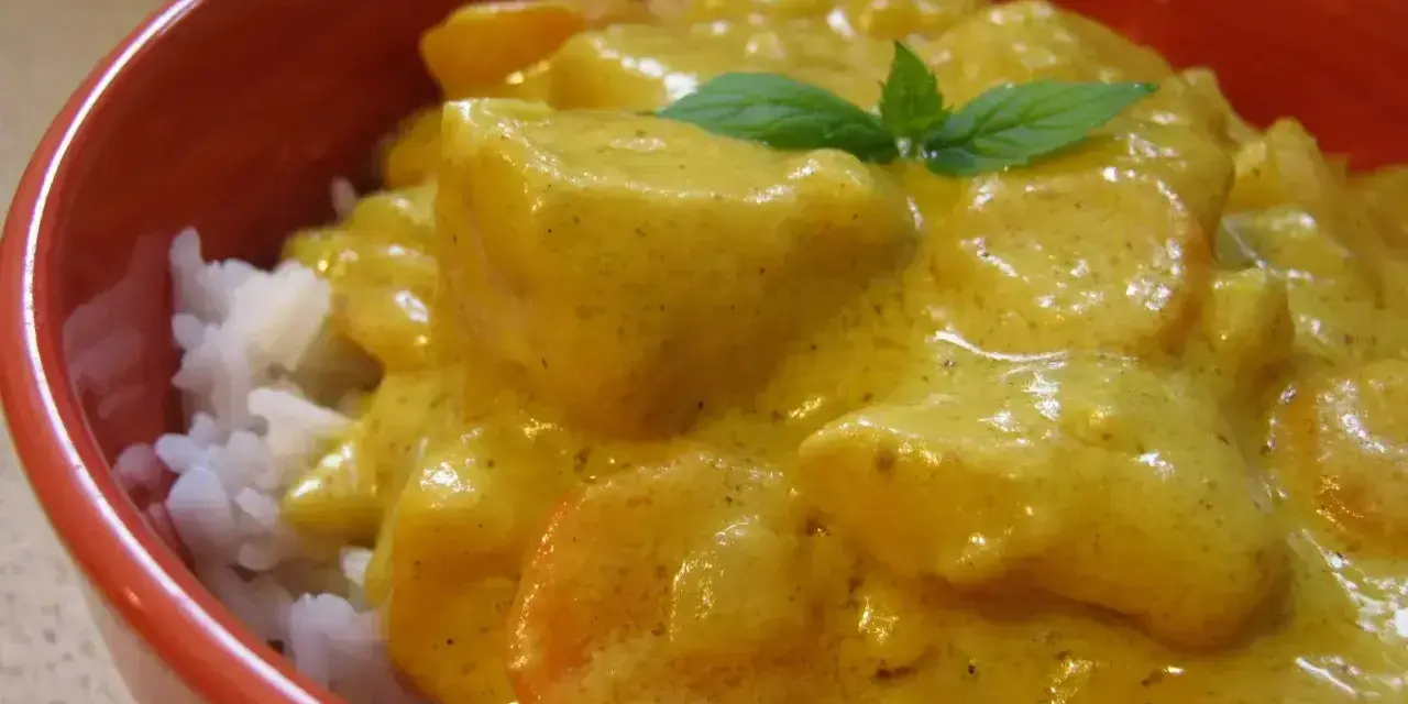 Miseczka ryżu z kurczakiem w kremowym sosie z curry, ozdobiona listkiem mięty.